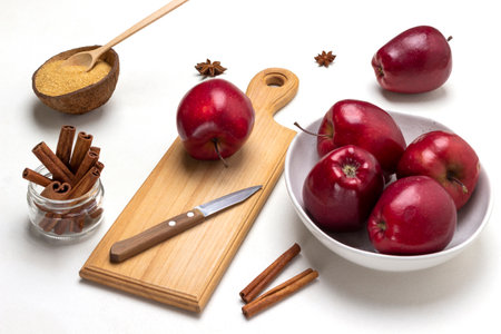Ripe red apples in a bowl. Apple and knife on cutting board. Cinnamon sticks in glass jar. top view. white backgroundの写真素材