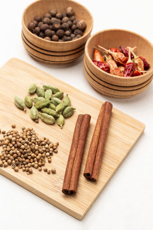 Cinnamon sticks, coriander seeds and cardamom on wooden board. Allspice and dry red pepper pods in wooden bowl. top view. white backgroundの写真素材