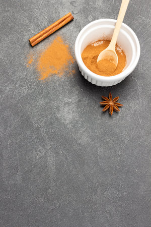 Ground cinnamon in porcelain bowl and spoon. Star anise and cinnamon stick on table. copyspace. flat lay. Black background.の写真素材