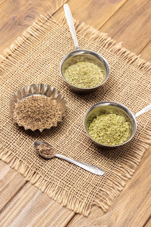 Dry rosemary, cilantro and cumin in spoon in metal bowls on burlap napkin. top view. wooden backgroundの写真素材