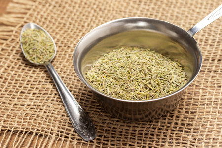 Dry rosemary in spoon and in metal bowl on burlap napkin. copyspace. top view. wooden backgroundの写真素材