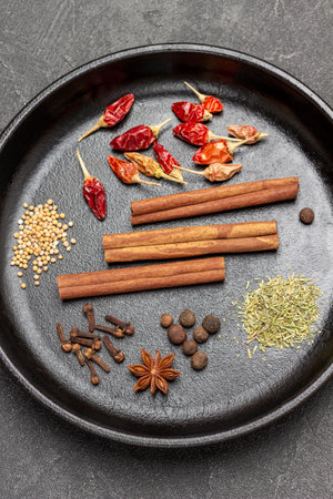 Cinnamon sticks, red pepper pods, star anise and cloves in frying pan. flat lay. black backgroundの写真素材