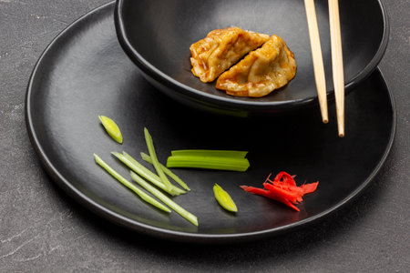 Chopped leek and pickled ginger on black plate. Boiled gyoza dumplings and chopsticks. top view. black backgroundの写真素材