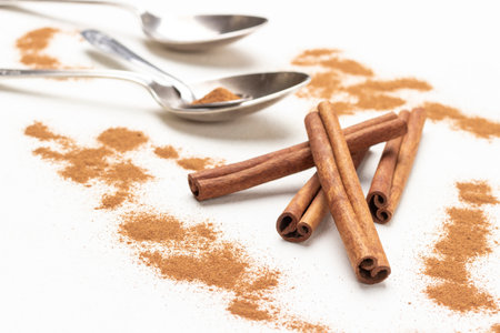 Cinnamon sticks among ground cinnamon, metal spoons on table. close up. top view. white backgroundの写真素材