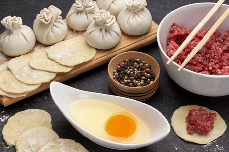 Ingredients for making dumplings and raw khinkali dumplings on board. Minced meat in bowl and chopsticks. Allspice and yolk in bowls. top view. black backgroundの写真素材