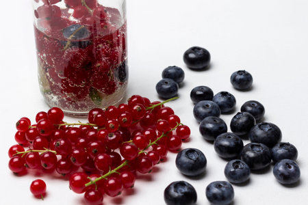 Sprigs of red currant and blueberries on the table. Summer berry drink in a bottle. white...