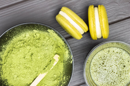 Two macarons and vatcha tea in a bowl. Green matcha tea powder in black bowl. flat lay. dark wooden backgroundの写真素材