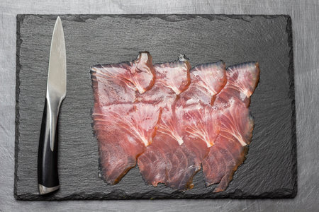 Thin slices of tuna and kitchen knife on stone board. flat lay. dark background.の写真素材