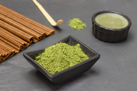 Matcha green tea powder in a bowl. Measuring spoon and green tea. gray background.