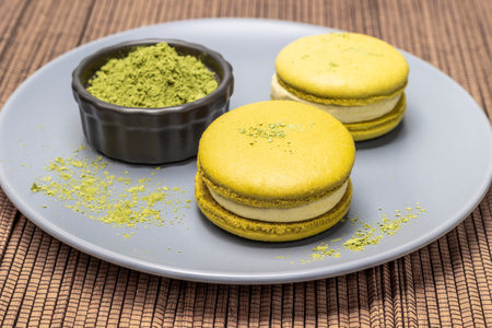 Macaron cakes and matcha tea powder on a gray plate and on a napkin made of wooden sticks. top viewの写真素材