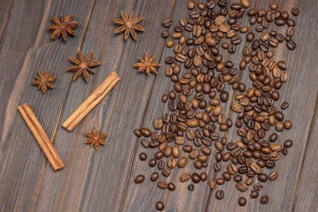 Coffee beans scattered on table, star anise, cinnamon sticks and pieces of brown sugar. Dark background. Flat layの写真素材