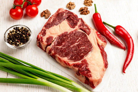 Raw meat. Marbled beef steak. Green onions, chili peppers, walnuts, on table. Organic food. Top...