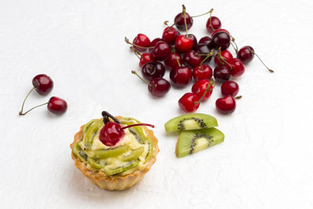 Tart decorated with red cherry and kiwi. Kiwi and red cherry on white background. Top view. Copy space.の写真素材