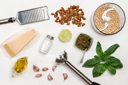 Pesto sauce. Cutter with pine nut, whiskey, grater, pesto bowl, basil leaves, parmesan, garlic, lemon. Flat lay. White backgroundの写真素材