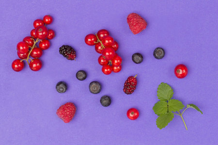 Still life of multi-colored berries on purple background. Red currents, raspberries red and yellow,...