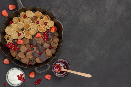Pancakes and berries in pan. Yogurt and jam on table. Black background. Flat lay. Copy spaceの写真素材