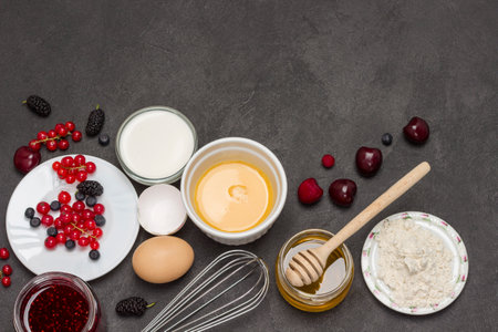 Whisk, bowl of broken eggs. Flour, berry milk, butter, honey jam. Ingredients for cooking breakfast. Copy space. Flat layの写真素材