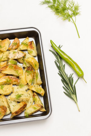 Baked potatoes in baking dish. Rosemary and green peppers, garlic and lemon on table. White background. Flat lay.の写真素材
