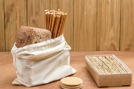 Bread and edible straw in linen bag. Bread in cardboard box. Ecological concept. Wood background.