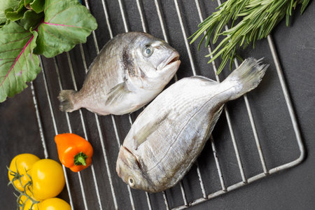 Raw dorado fish with yellow vegetables on metal grill grate. Black background. Top viewの写真素材