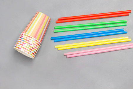 Colorful paper cups and colorful plastic straws for drinks. Gray background. Flat lay. Reuse, environmental concept.の写真素材