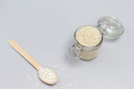 Three types of white rice in glass jar, wooden spoon and bowl. Top view. Gray backgroundの写真素材