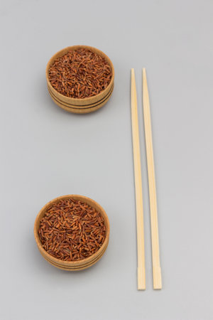 Red brown rice in wooden bowl. Sticks on gray background. Flat layの写真素材