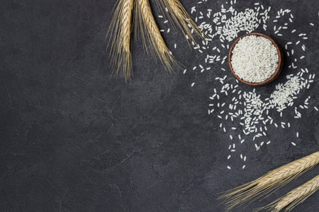 Glutinous rice in wooden bowl. Sprigs of cereals and sprinkled rice on table. Copy space. Black background. Flat layの写真素材