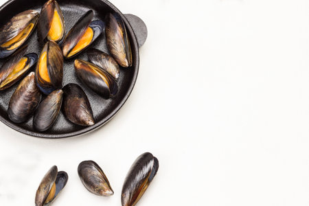 Shellfish Mussels in frying pan. Mussels are scattered on table. Copy space. Flat lay. White backgroundの写真素材