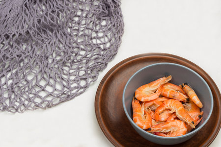 Shrimp in gray bowl. Gray mesh, allspice and lemon on table. White background. Top viewの写真素材
