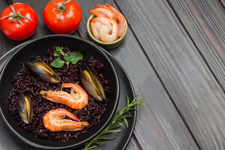 Shrimps and mussels with black rice on plate. Tomatoes, shrimps in bowl. Dark wooden background. Copy space. Top viewの写真素材