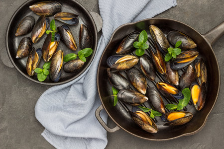 Raw mussels in shells with mint in frying pan. Gray napkin between two pans. Black background. Flat layの写真素材