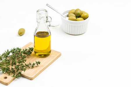 Olive oil bottle and thyme sprigs on board. Olives in ceramic bowl. Copy space. White background. Top view.の写真素材