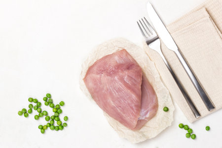 Diet turkey meat with green peas. Knife and fork on napkin. Balanced diet. Copy space. White background. Flat lay.の写真素材