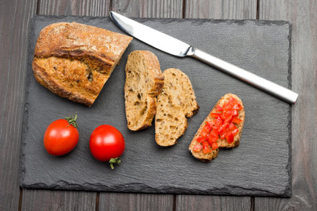 Pieces of bread and knife. Sliced tomato sandwich. Delicious snack and appetizer. Dark wooden background. Top viewの写真素材