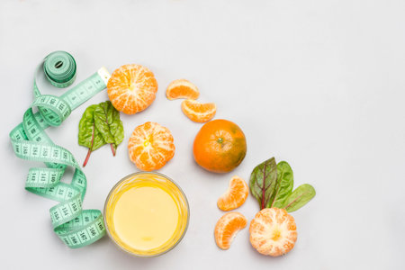 Tangerine fruits, citrus juice in glass and measuring tape. Gray background. Flat lay. Copy spaceの写真素材