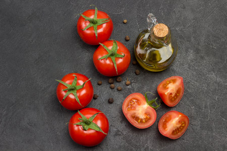 Whole tomato and chopped tomato wedges, all spice on table. Bottle of olive oil and sprig of rosemary. Black background. Top view.の写真素材