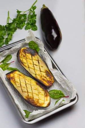 Grilled baked eggplants on pallet. Whole eggplant, onion and parsley on table. Gray background. Top view.の写真素材