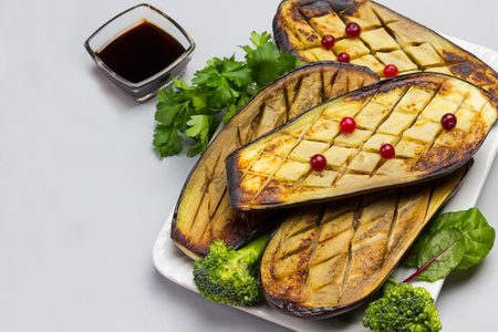 Baked eggplant with parsley and broccoli. Sauce in bowl and cranberries on table. Gray background. Top viewの写真素材