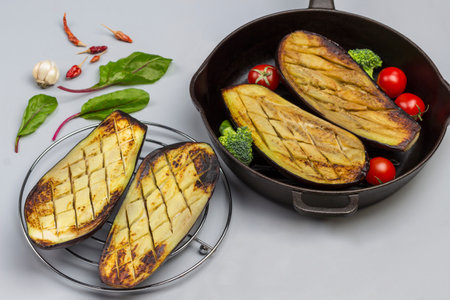 Grilled eggplants on wire rack and in frying pan. Chard leaves and garlic on the table. Gray background. Top viewの写真素材