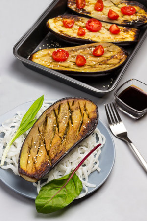 Baked eggplant with greens and rice noodles on plate. Baked eggplant with tomatoes in pallet. Sauce in glass bowl. Top viewの写真素材