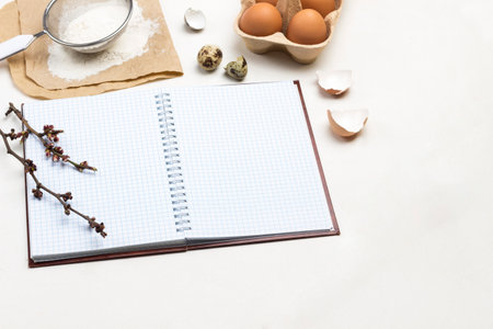Notebook on spring. Two wooden spoons. Chicken eggs and chicken shells. Flour and sit on paper. White background. Top view.の写真素材