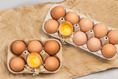 Brown chicken eggs in carton container. Broken eggs in container. Eggshell on table. Brown background from crumpled paper. Flat layの写真素材