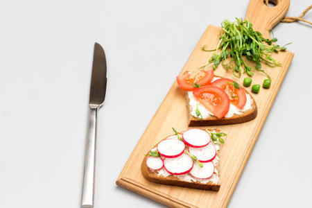 Vegetarian sandwiches with tomatoes and radishes on cutting board. Microgreen pea sprouts. Knife and half tomato on table. Gray background. Flat lay. Copy spaceの写真素材
