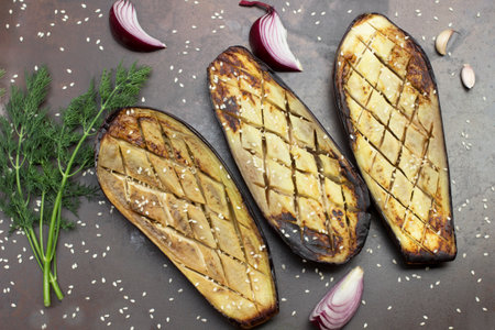 Baked eggplant with onions, garlic and sesame seeds. Sprig of dill. Rusty metal background. Top viewの写真素材