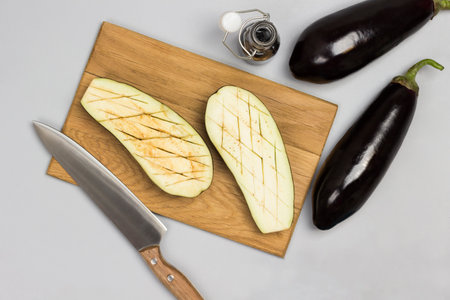 Eggplant halves on cutting board. Whole eggplants, napkin and sauce on table. Gray background. Flat lay.の写真素材