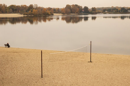 A volleyball net on an empty beach. A man is sitting on a bench.の写真素材