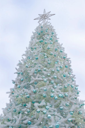 Silver Christmas tree with turquoise New Year's toys. A star on the top of the tree against the sky.の写真素材