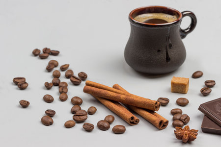 Coffee drink in black cup. Cinnamon sticks, pieces of chocolate and coffee grains on table. Gray background. Top viewの写真素材