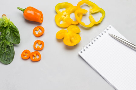 Sliced yellow peppers and spinach leaves. Pen and notebook. Gray background. Top view